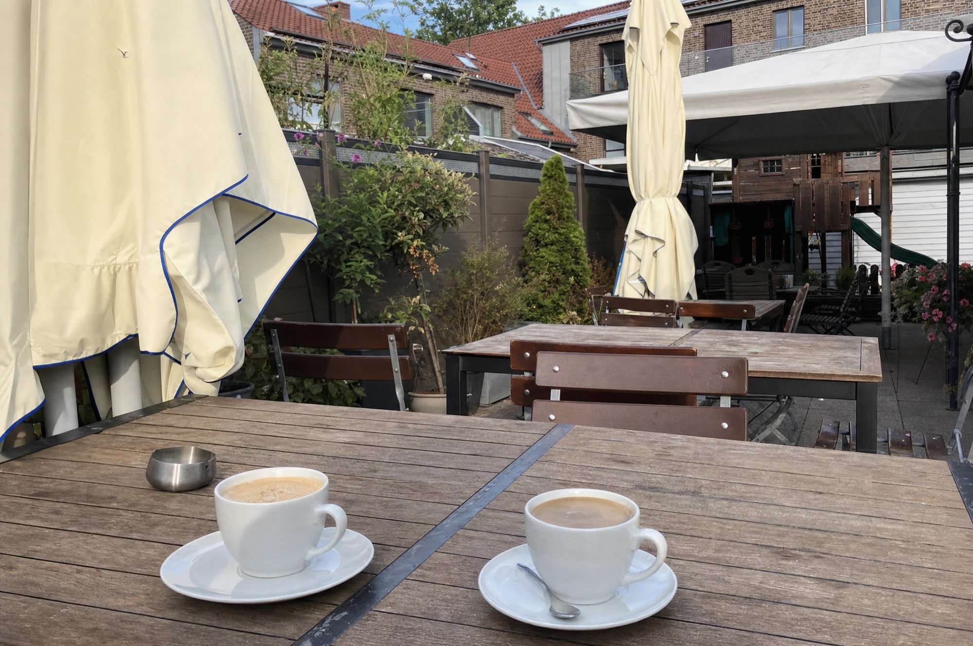 Idyllischer Biergarten mit Holztischen, Sonnenschirmen und Lichterketten im Abendlicht